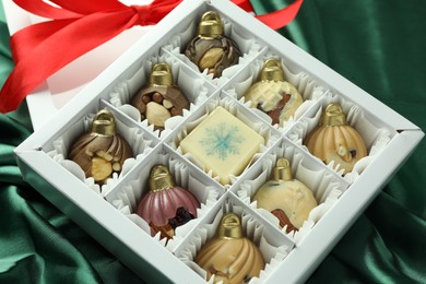 Photo of Box with tasty sweets in shape of baubles on green fabric background, closeup