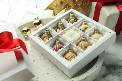 Photo of Box with tasty sweets in shape of baubles and Christmas decor on white marble background, closeup