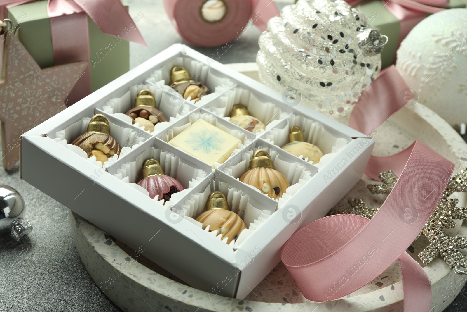 Photo of Box with tasty sweets in shape of baubles and Christmas decor on grey background, closeup