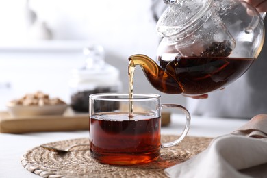 Photo of Woman pouring hot black tea into cup at white table, closeup