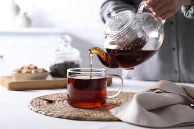 Photo of Woman pouring hot black tea into cup at white table, closeup