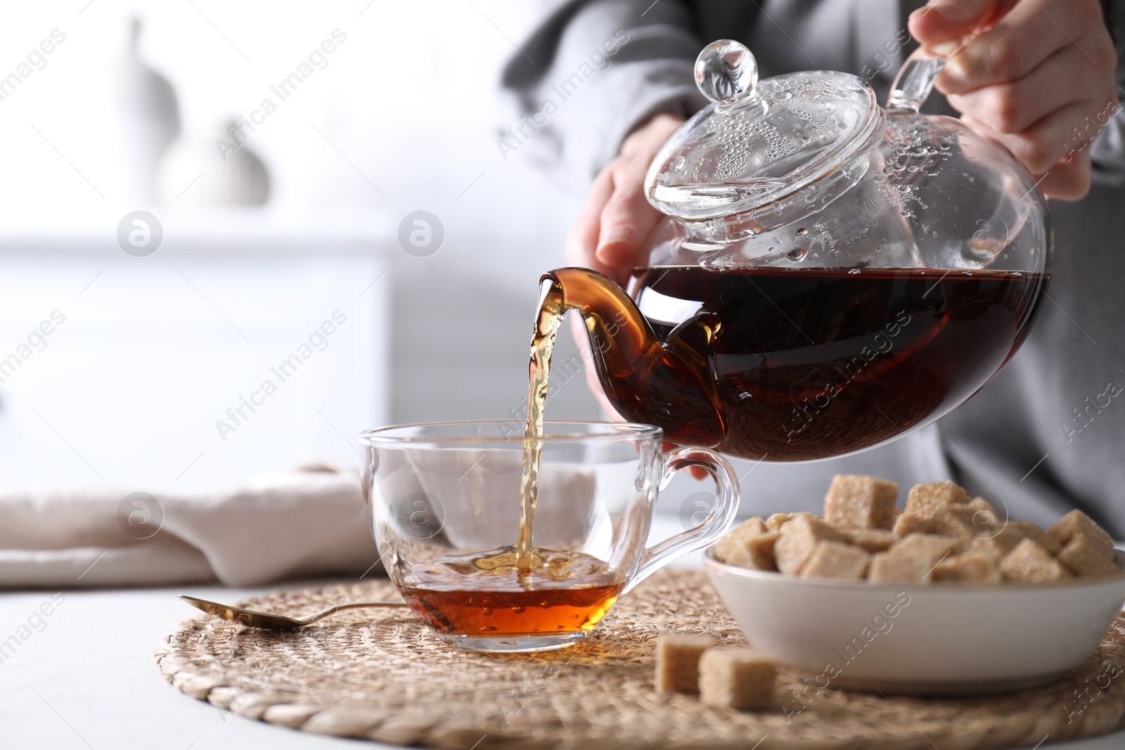 Photo of Woman pouring hot black tea into cup at white table, closeup