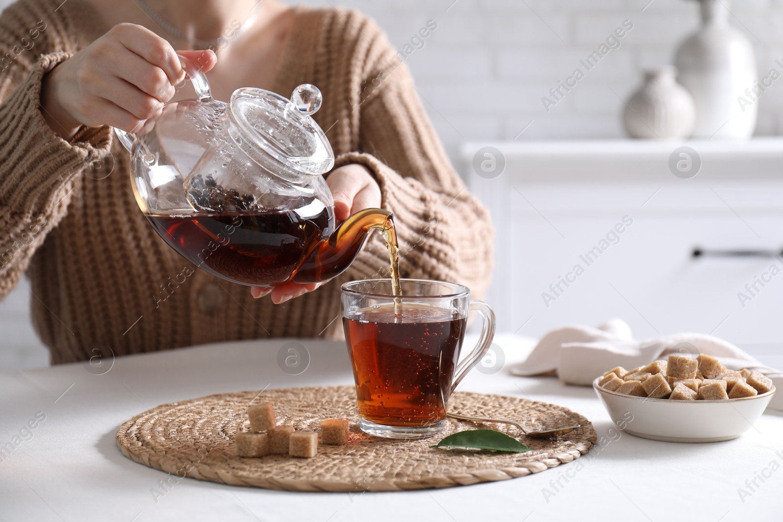 Photo of Woman pouring hot black tea into cup at white table, closeup