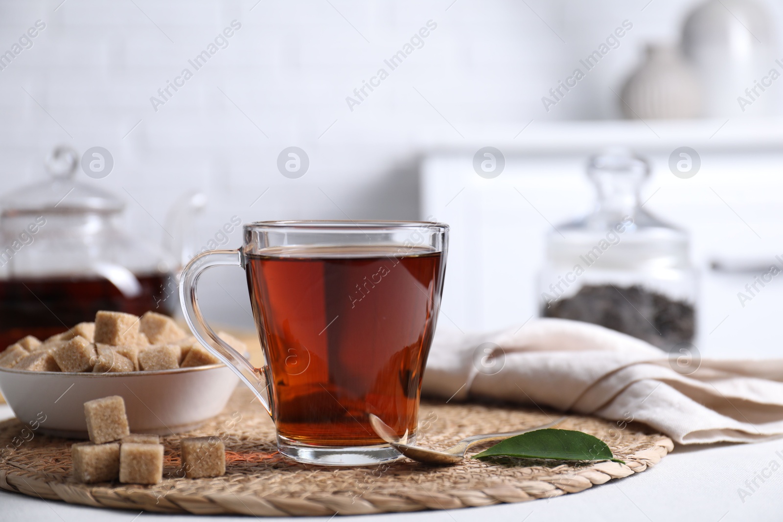 Photo of Aromatic black tea in cup and brown sugar cubes on white table