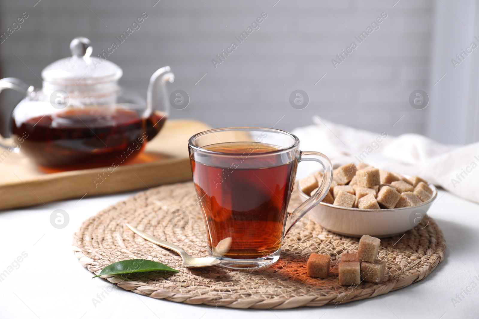 Photo of Aromatic black tea in cup and brown sugar cubes on white table