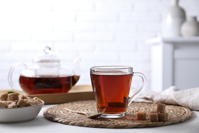 Photo of Aromatic black tea in cup and brown sugar cubes on white table