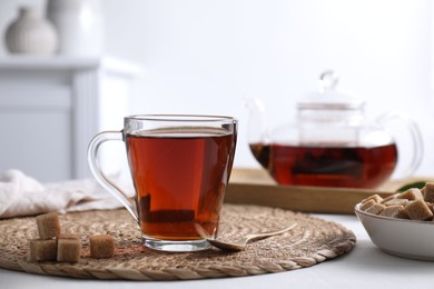 Photo of Aromatic black tea in cup and brown sugar cubes on white table