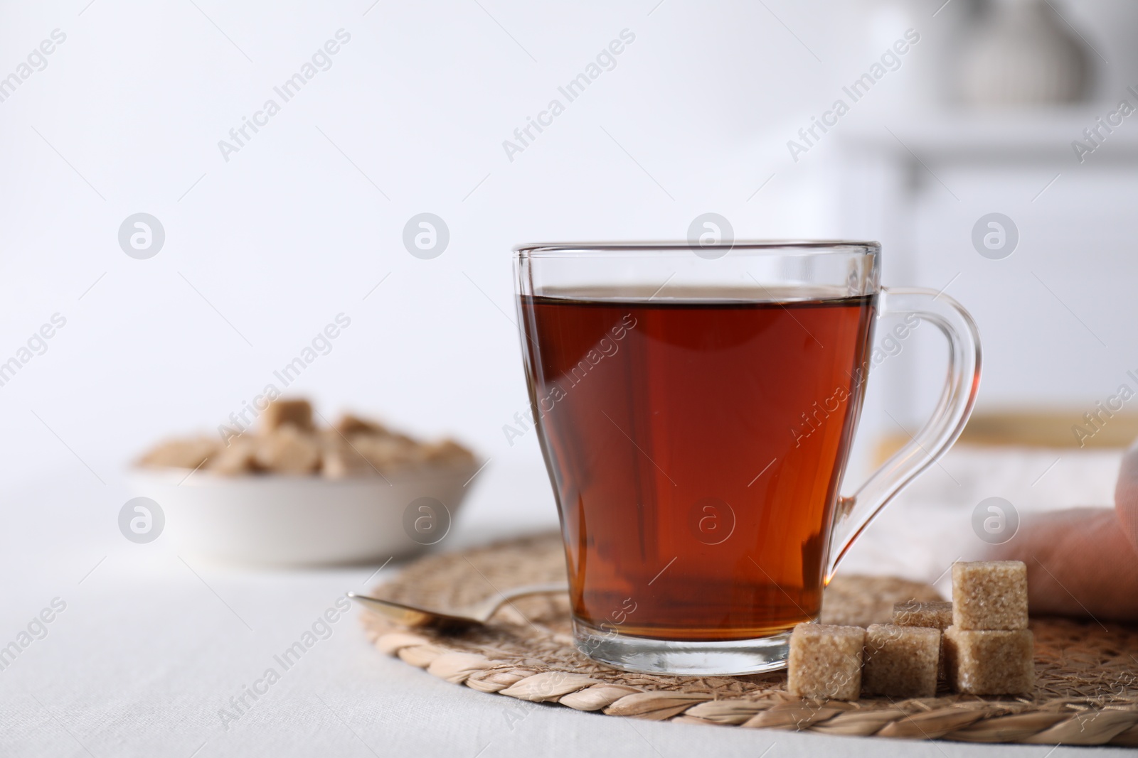 Photo of Aromatic black tea in cup and brown sugar cubes on white table, closeup. Space for text