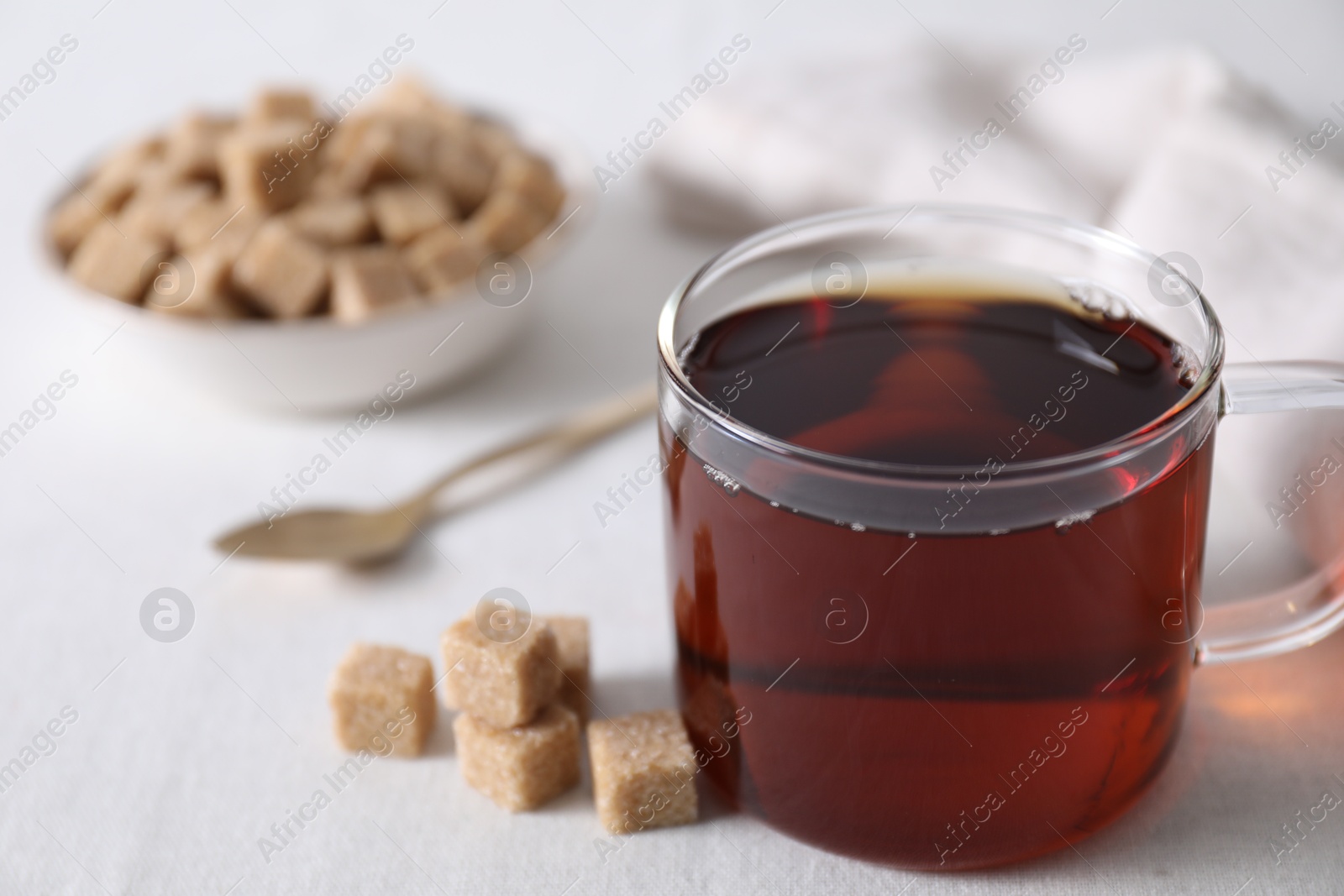 Photo of Aromatic black tea in cup and brown sugar cubes on white table, closeup