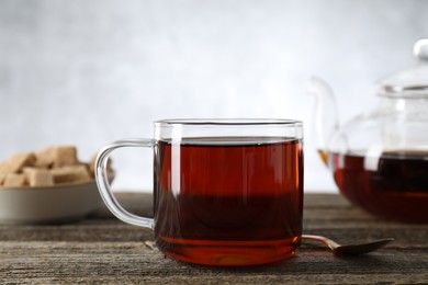 Photo of Aromatic black tea in cup and spoon on wooden table, closeup