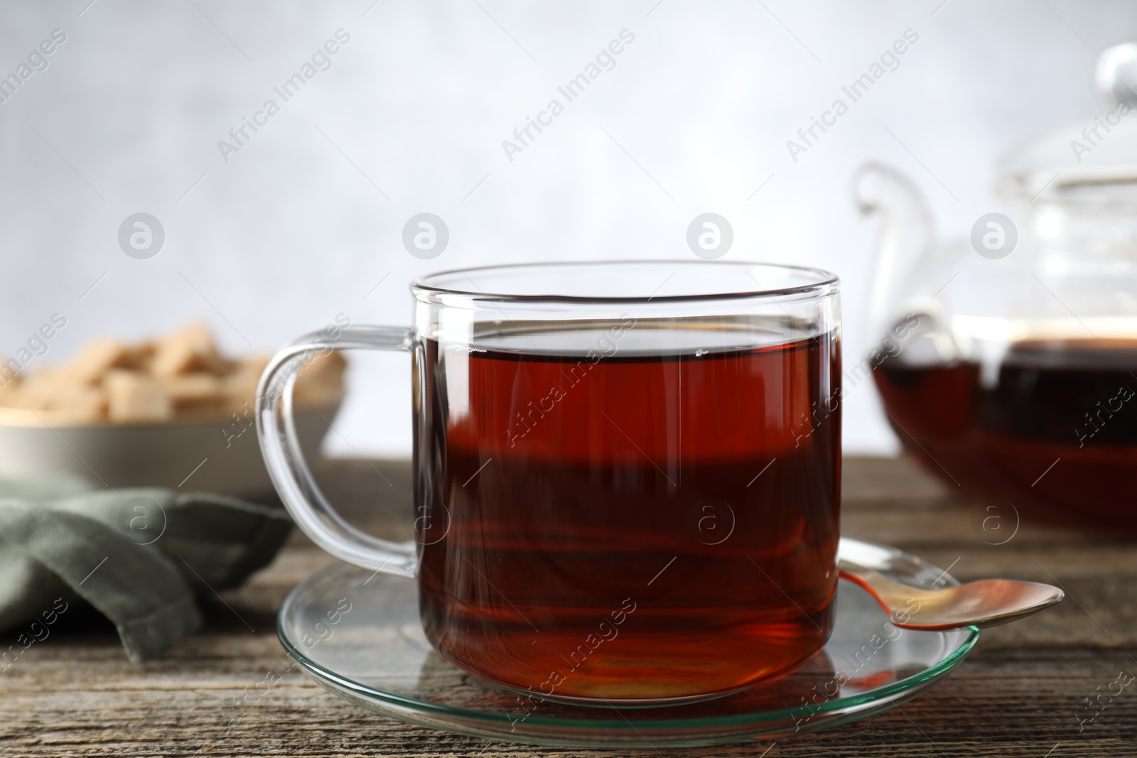 Photo of Aromatic black tea in cup and spoon on wooden table, closeup