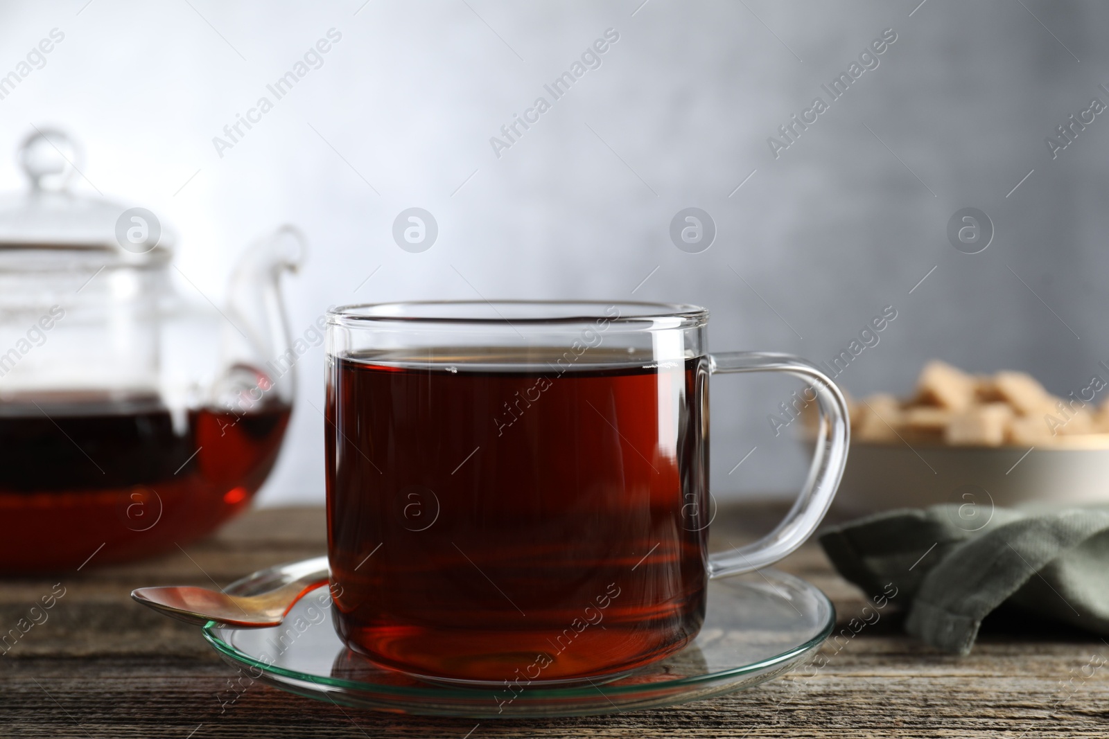 Photo of Aromatic black tea in cup and spoon on wooden table, closeup