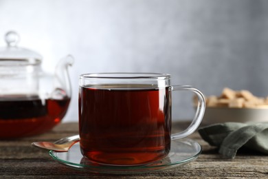 Photo of Aromatic black tea in cup and spoon on wooden table, closeup