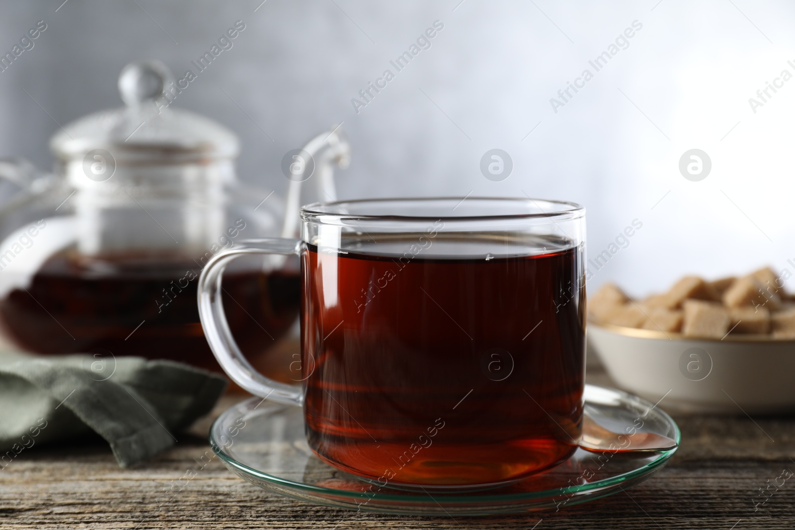 Photo of Aromatic black tea in cup and spoon on wooden table, closeup