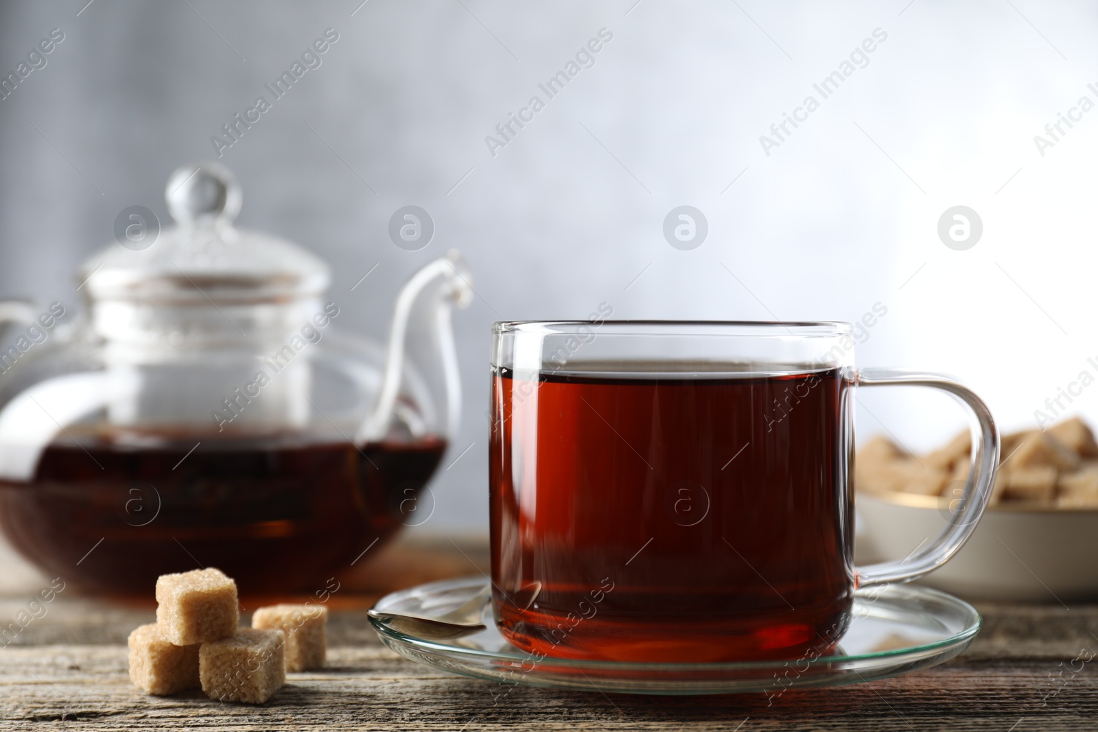 Photo of Aromatic black tea in cup and brown sugar cubes on wooden table, closeup