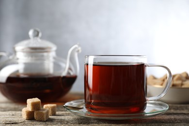 Photo of Aromatic black tea in cup and brown sugar cubes on wooden table, closeup