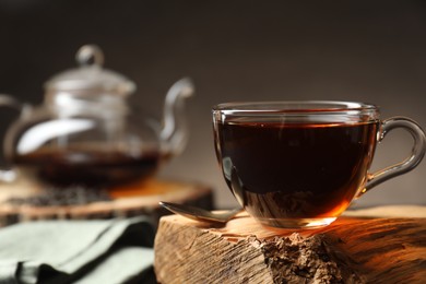 Photo of Aromatic black tea in cup on wooden snag, closeup