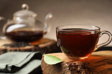 Photo of Aromatic black tea in cup and green leaf on wooden snag, closeup