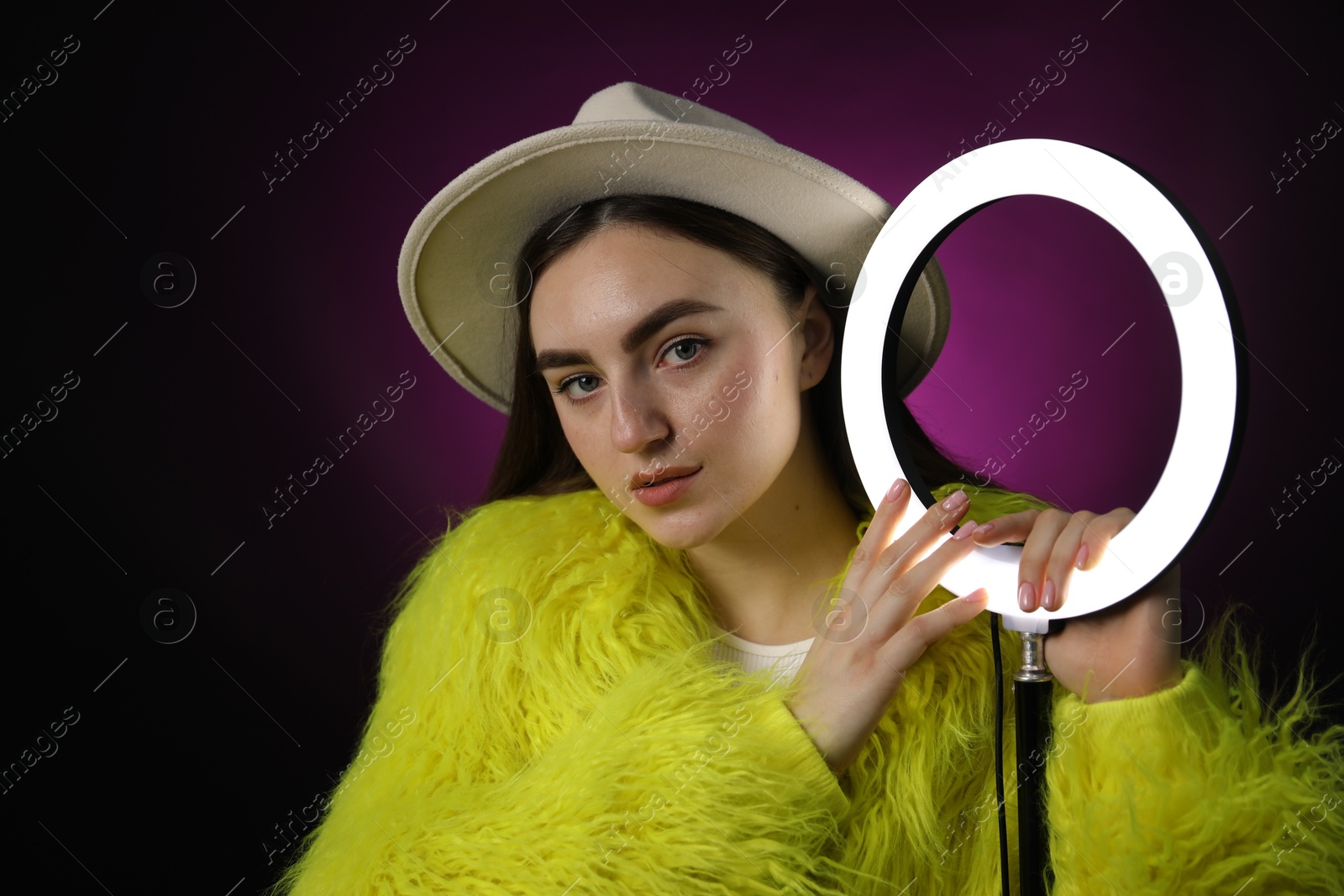 Photo of Stylish woman with ring lamp on dark purple background