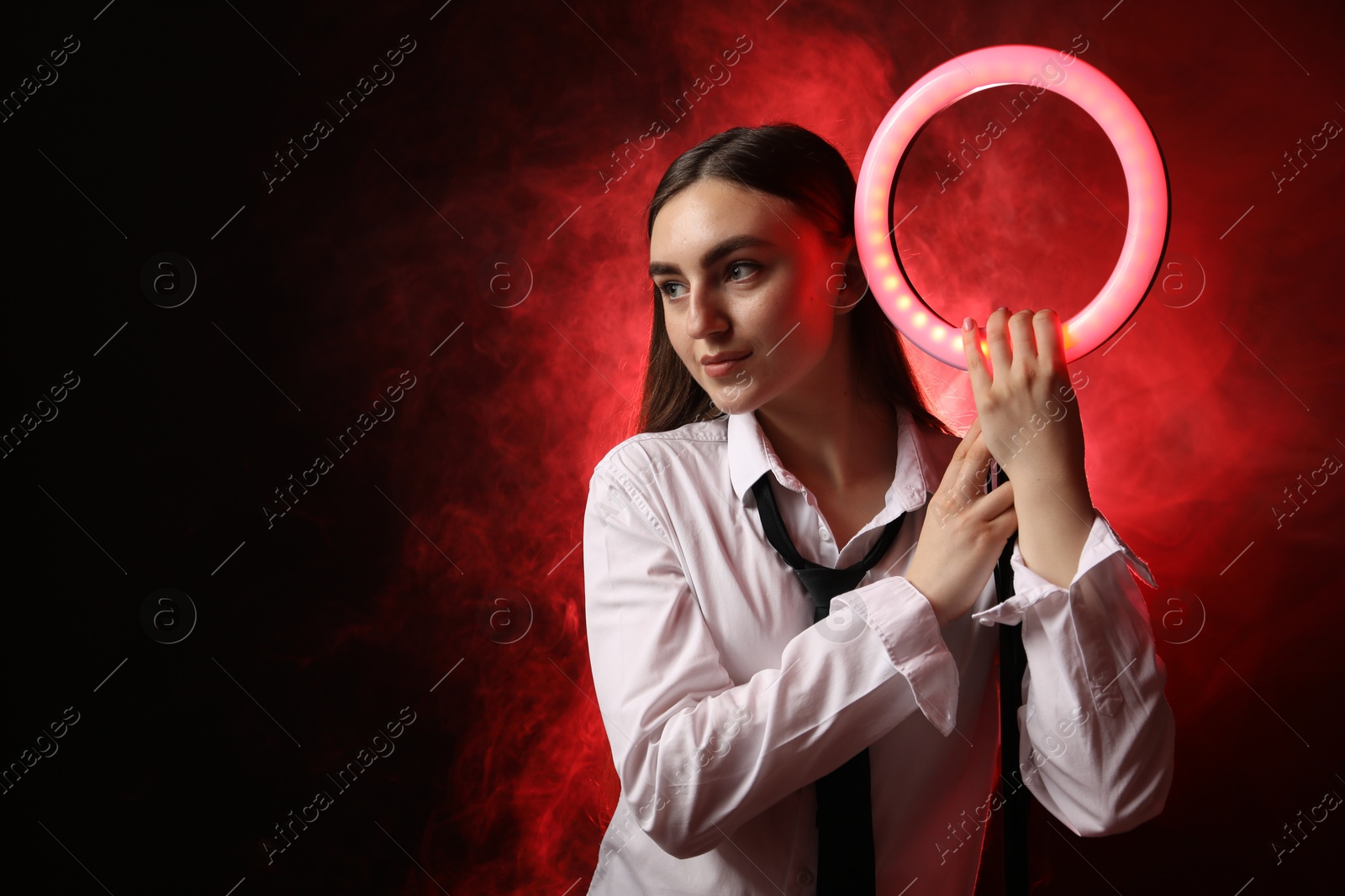 Photo of Beautiful woman with ring lamp on dark red background in smoke, space for text