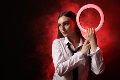 Photo of Beautiful woman with ring lamp on dark red background in smoke, space for text