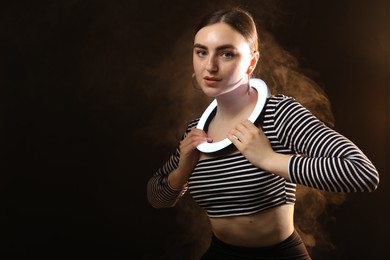 Photo of Beautiful woman with ring lamp on dark background in smoke, space for text