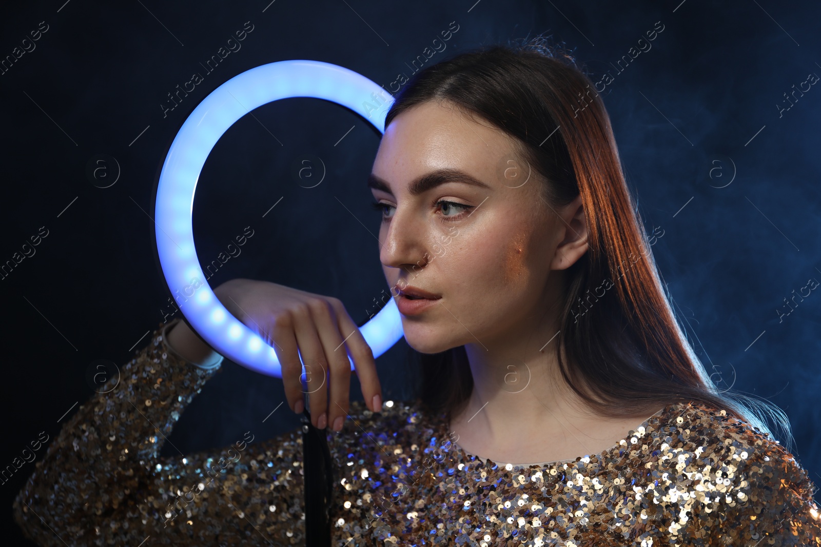 Photo of Beautiful woman with ring lamp on dark blue background in smoke