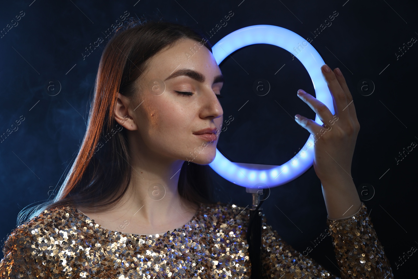 Photo of Beautiful woman with ring lamp on dark blue background in smoke