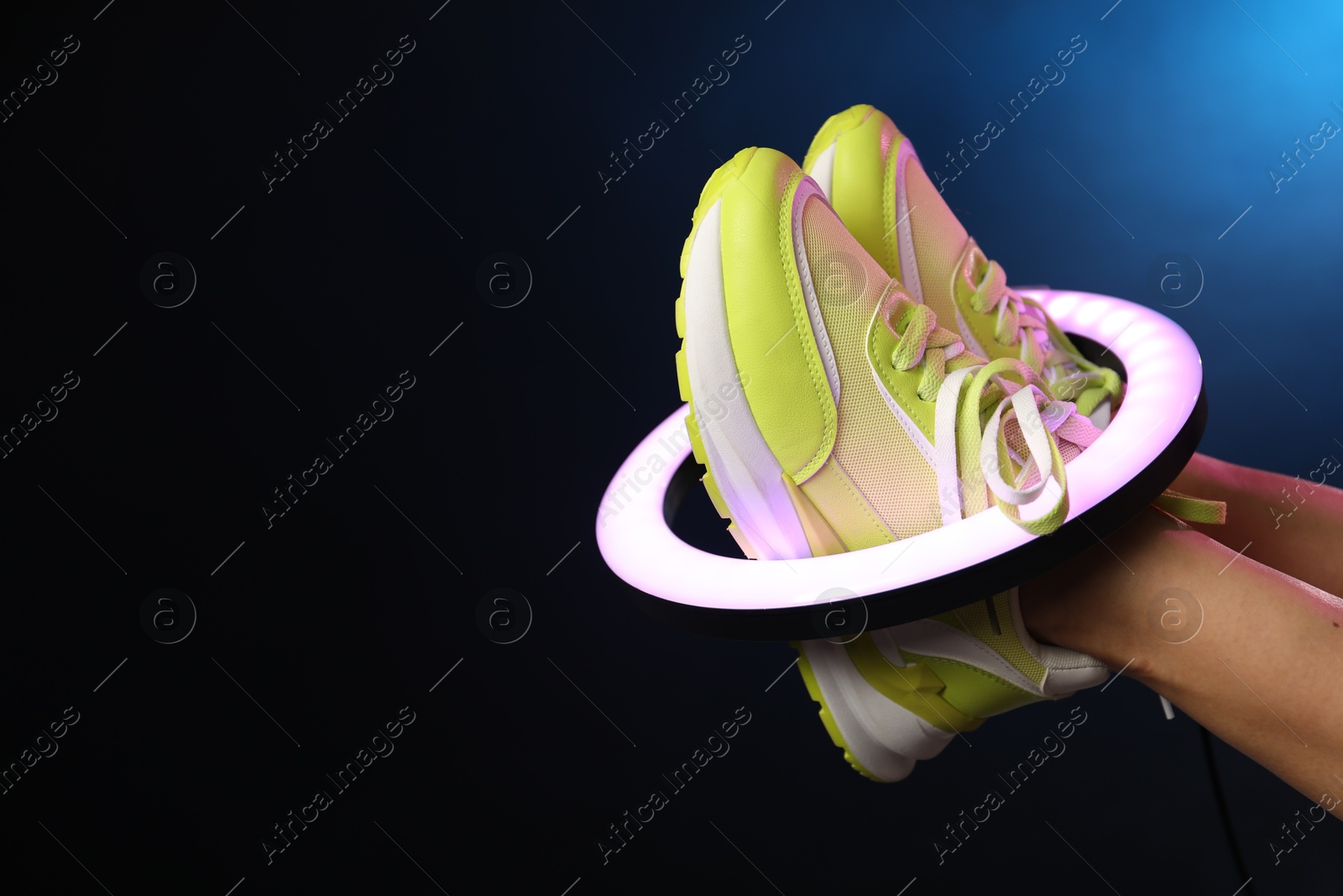 Photo of Woman with ring lamp wearing sneakers on dark blue background, closeup. Space for text