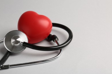 Photo of Cardiology. Stethoscope and red decorative heart on light gray background, closeup. Space for text