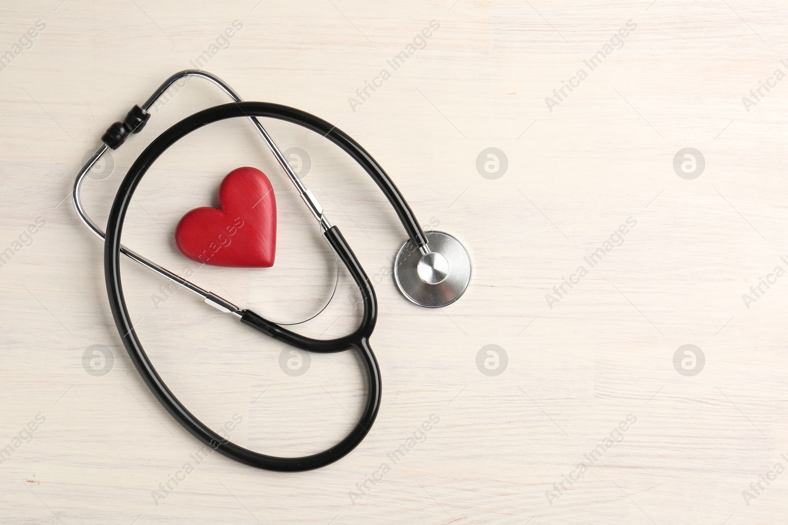 Photo of Cardiology. Stethoscope and red decorative heart on light wooden table, flat lay. Space for text