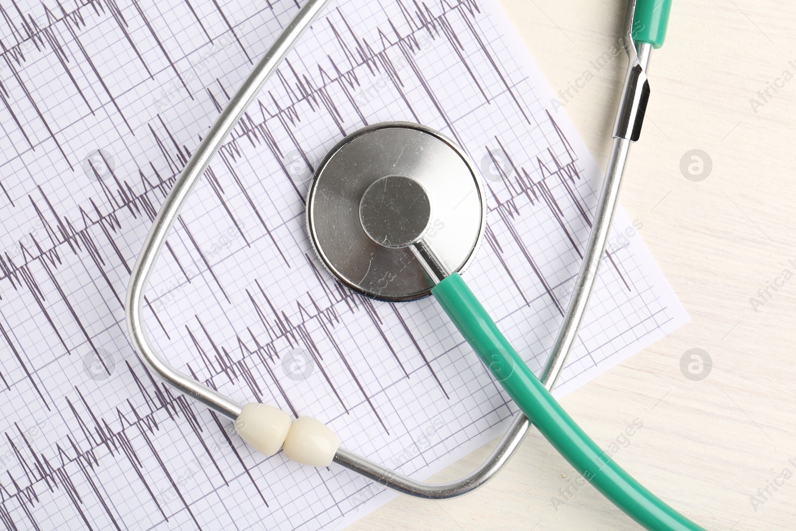 Photo of Cardiology. Stethoscope and cardiogram on light wooden table, top view