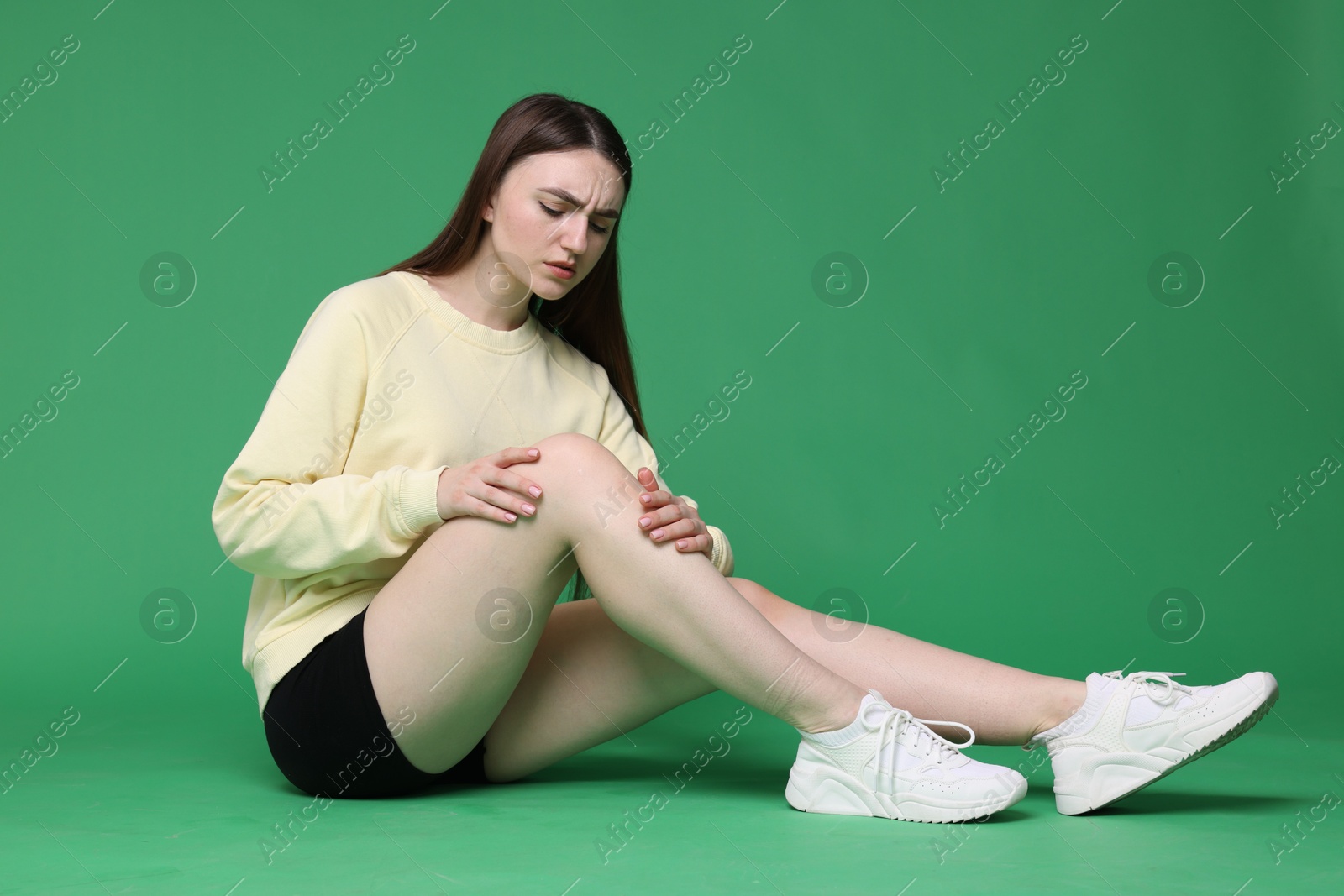 Photo of Young woman suffering from pain in knee on green background