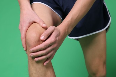 Photo of Young man suffering from pain in knee on green background, closeup