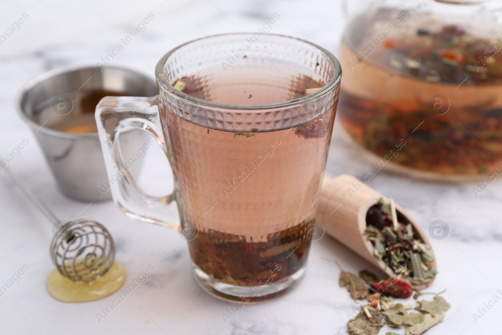 Photo of Delicious herbal tea with honey and dry leaves on white marble table, closeup