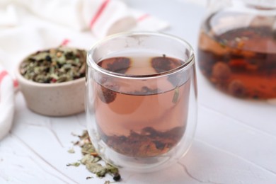 Photo of Delicious herbal tea and dry leaves on white table, closeup