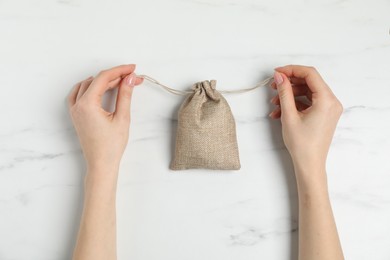 Photo of Woman with burlap bag at white marble table, top view