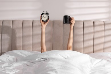 Photo of Woman with alarm clock and cup in bed at home, closeup. Good morning