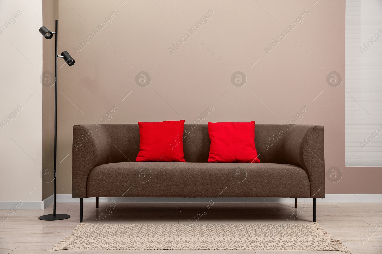 Image of Sofa in mocha mousse shade with pillows and floor lamp indoors. Cozy living room interior with trendy color of 2025 year