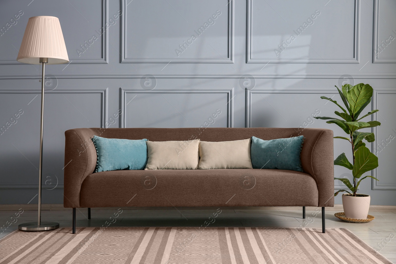 Image of Sofa in mocha mousse shade with pillows, houseplant and floor lamp indoors. Cozy living room interior with trendy color of 2025 year