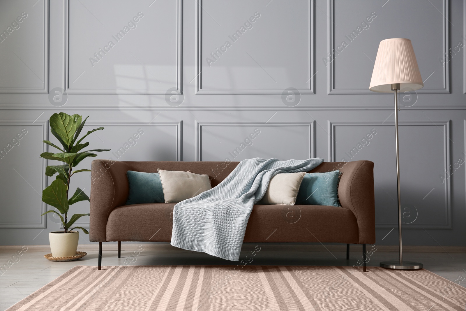 Image of Sofa in mocha mousse shade with pillows, houseplant and floor lamp indoors. Cozy living room interior with trendy color of 2025 year