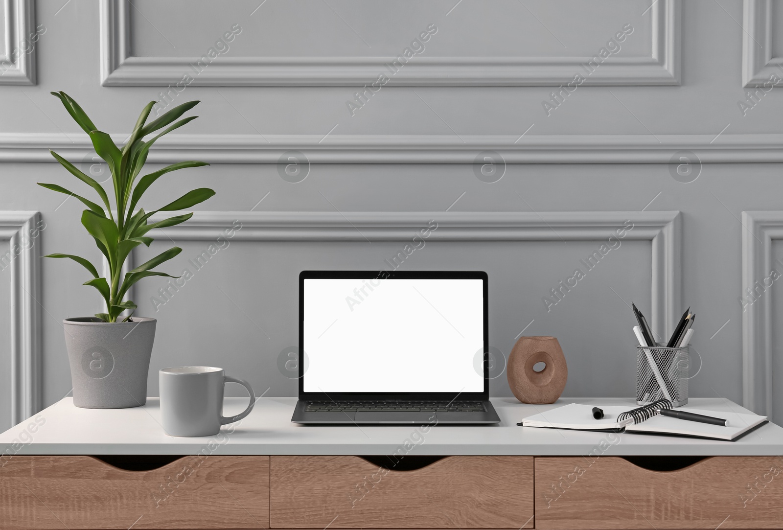 Image of Comfortable workplace with laptop, houseplant and stationery on table. Drawers in mocha mousse shade. Trendy color of 2025 year in interior design