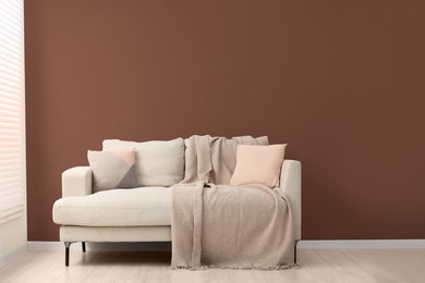 Image of Beige sofa with pillows and blanket near mocha mousse shade wall indoors. Interior with trendy color of 2025 year