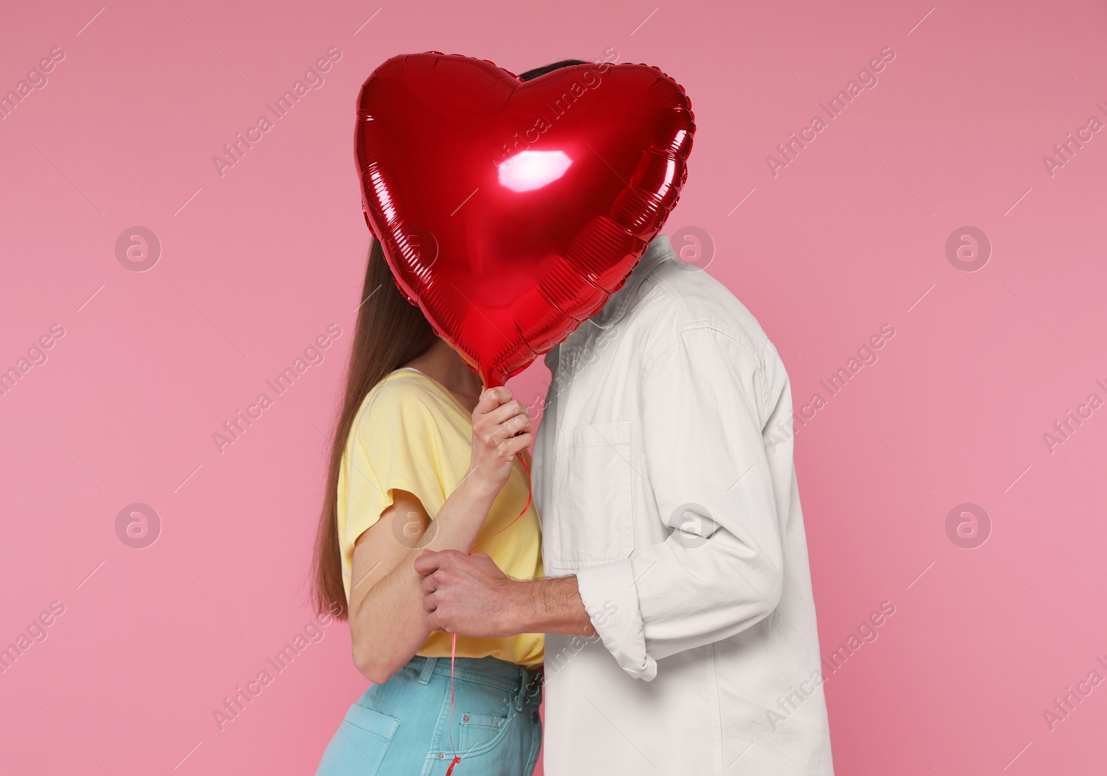 Photo of Lovely couple kissing behind heart shaped balloon on pink background. Valentine's day celebration