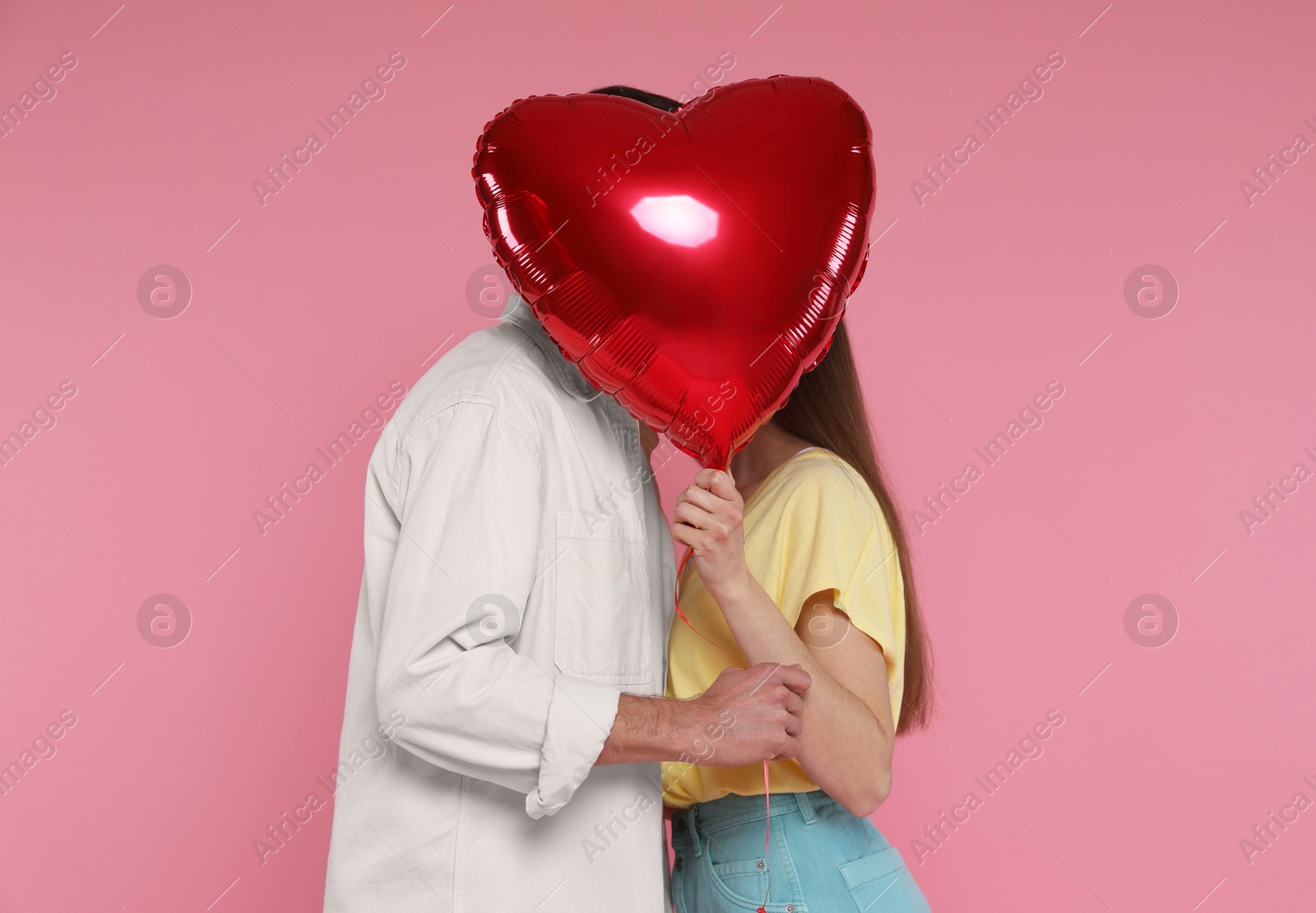 Photo of Lovely couple kissing behind heart shaped balloon on pink background. Valentine's day celebration