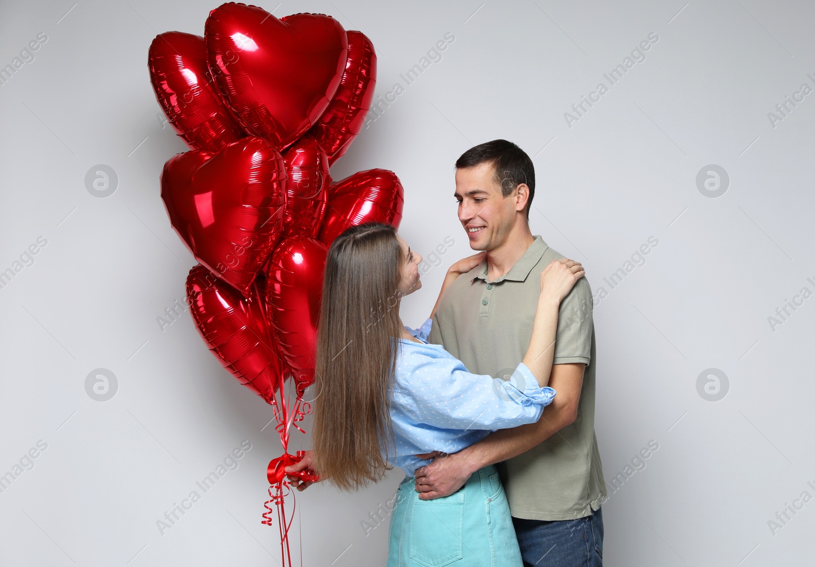 Photo of Lovely couple with heart shaped balloons on light background. Valentine's day celebration