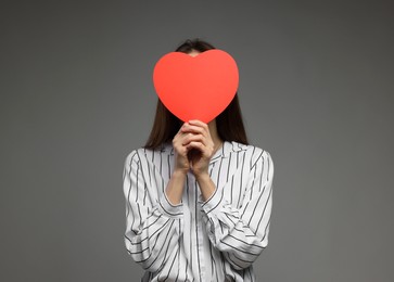 Photo of Happy Valentine's Day. Woman hiding behind paper heart on grey background