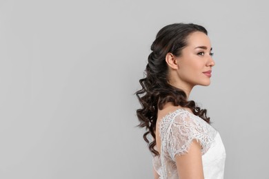 Photo of Young bride with beautiful wedding hairstyle on light grey background. Space for text