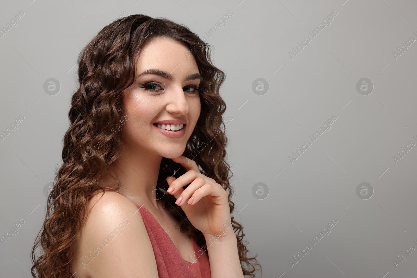 Photo of Beautiful young woman with long curly brown hair on grey background, space for text