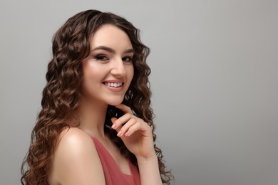 Photo of Beautiful young woman with long curly brown hair on grey background, space for text